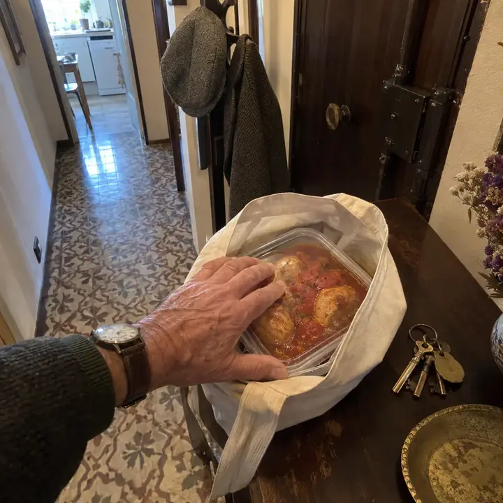 Táper de pollo al chilindrón metido en una bolsa de tela sobre el mueble del recibidor, junto a unas llaves