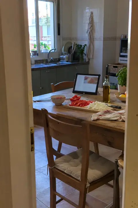 Tableta con una receta sobre la mesa de la cocina, junto a una tabla con pimiento rojo y cebolla cortados